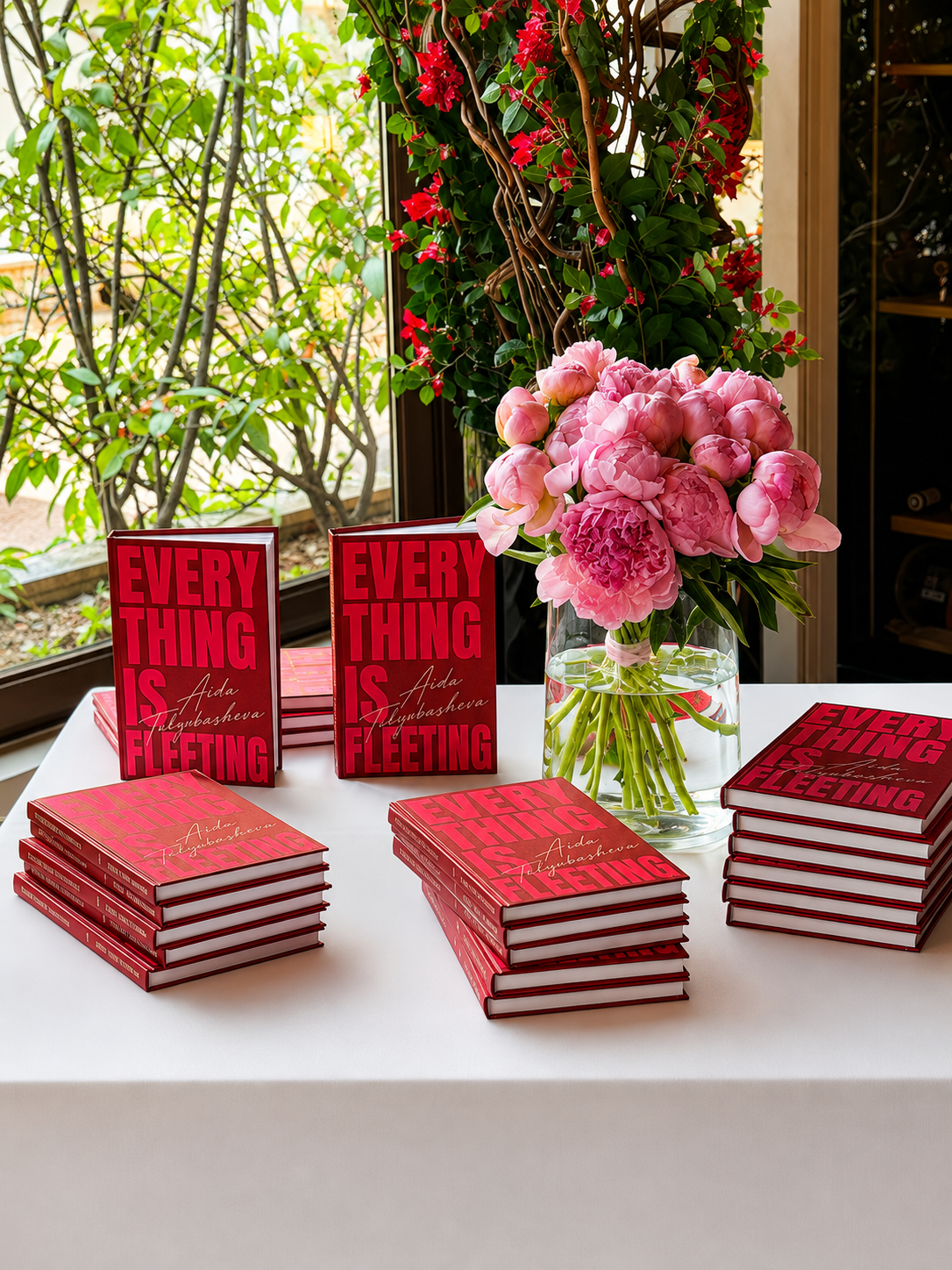 Signed editions of Everything Is Fleeting arranged with fresh peonies