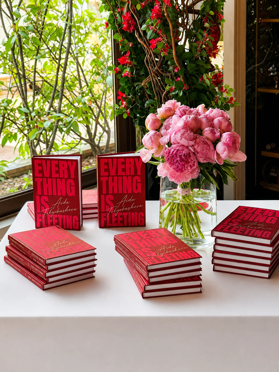 Signed editions of Everything Is Fleeting arranged with fresh peonies