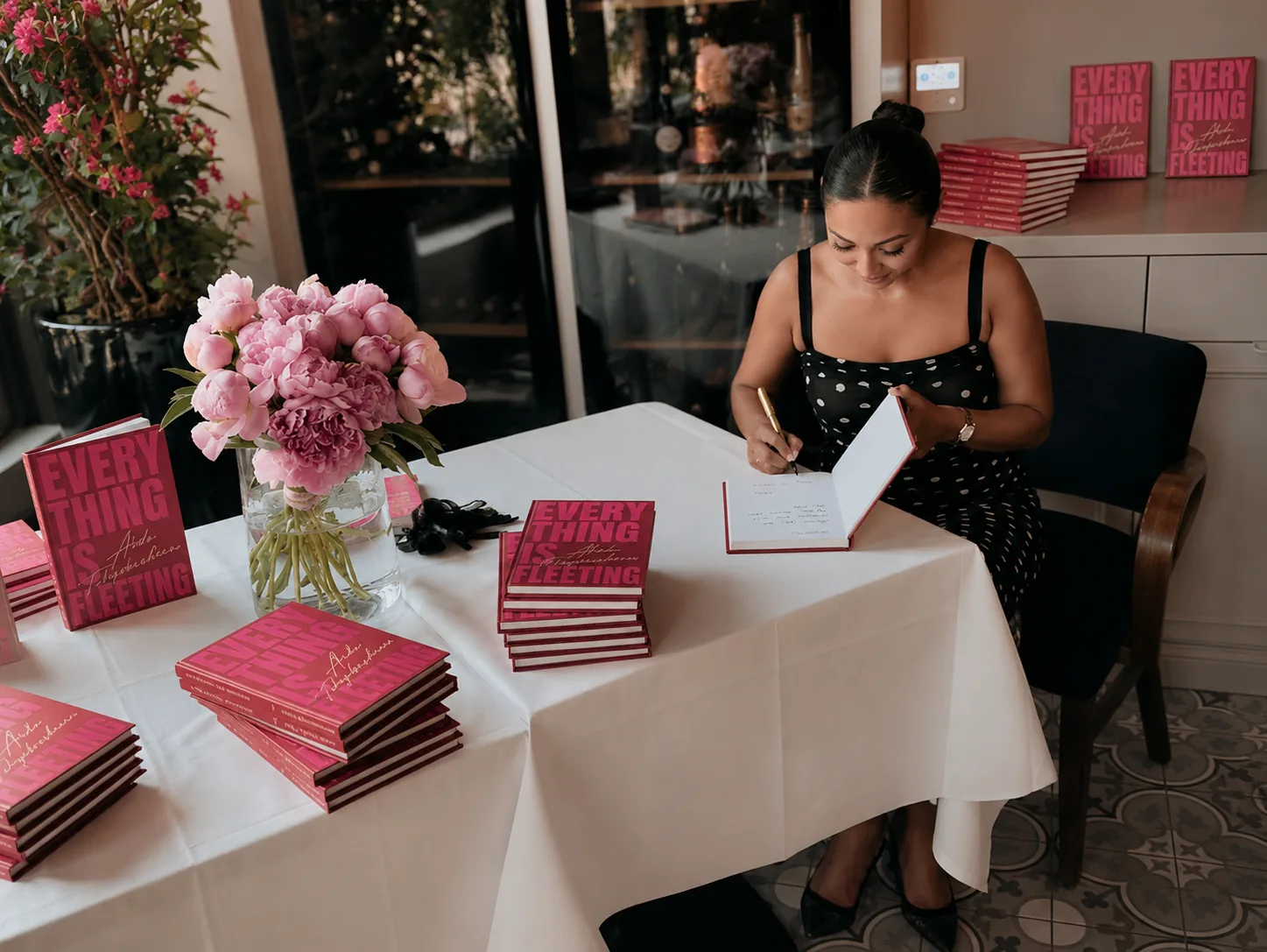 Aida Takyrbasheva signing copies of Everything Is Fleeting at a table with pink peonies